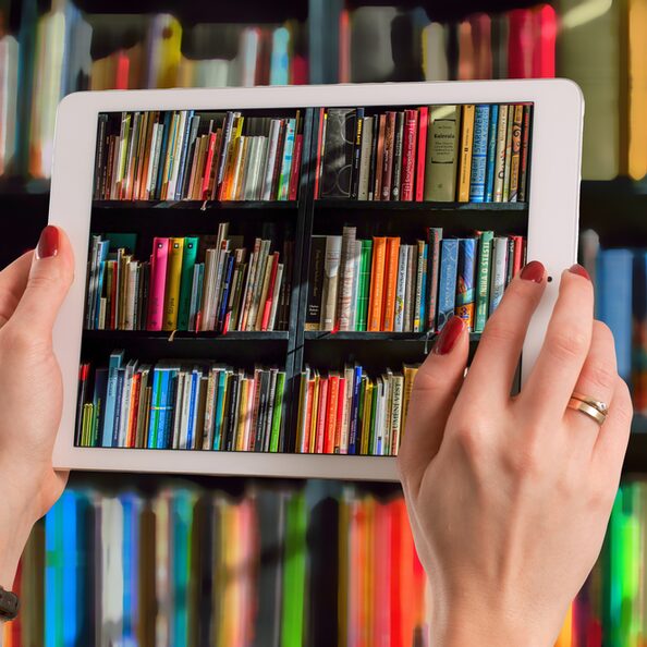 Hände halten Tablet mit Büchern im Hintergrund